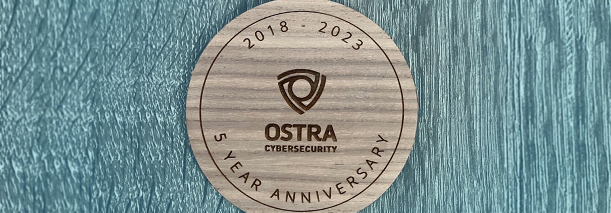 round wood plaque on blue stained wood background commemorating Ostra Cybersecurity's 5 year anniversary