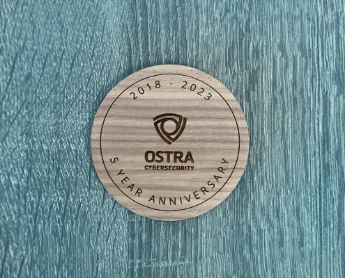 round wood plaque on blue stained wood background commemorating Ostra Cybersecurity's 5 year anniversary